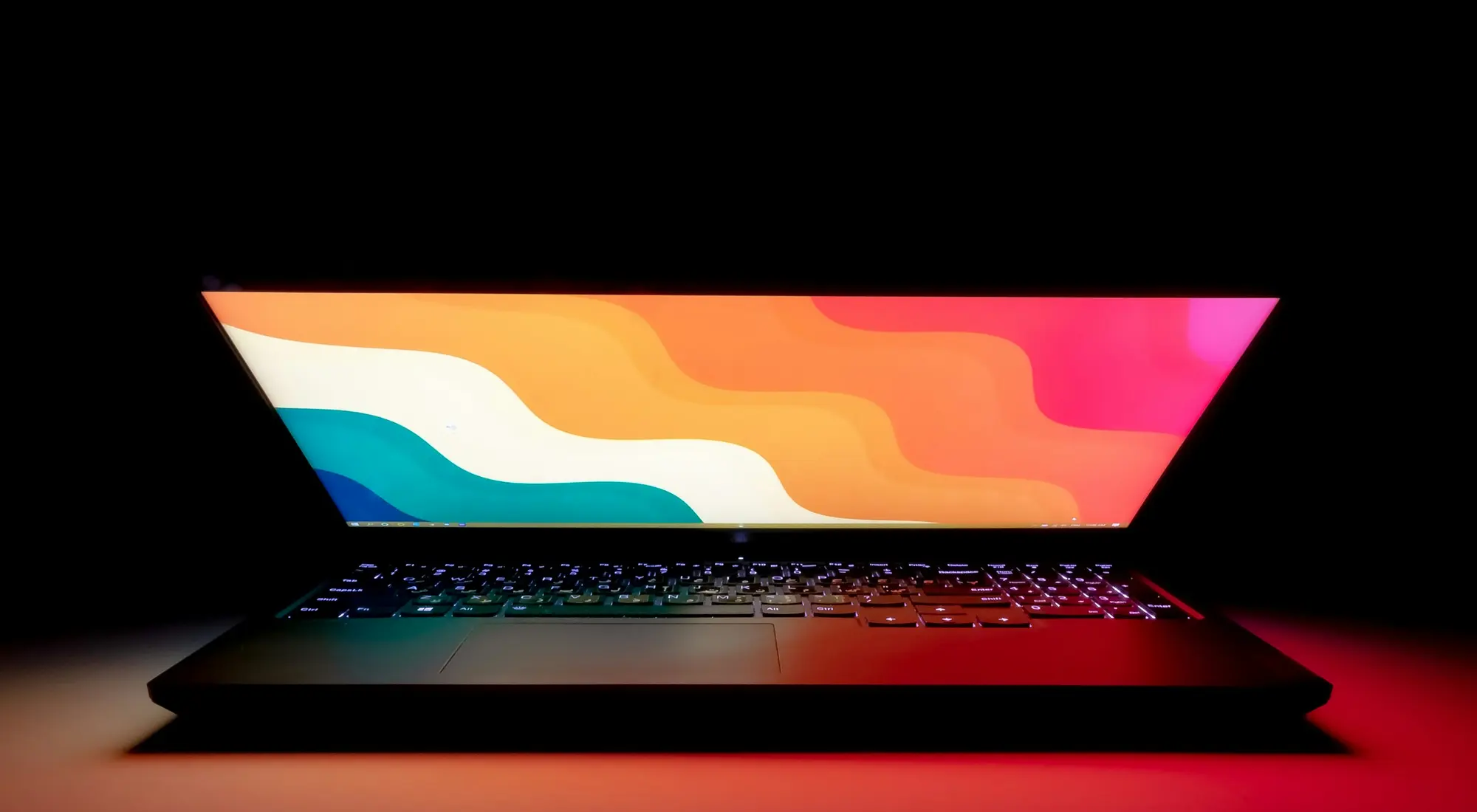 A laptop open on a dark desk, the lid lit by its own screen.