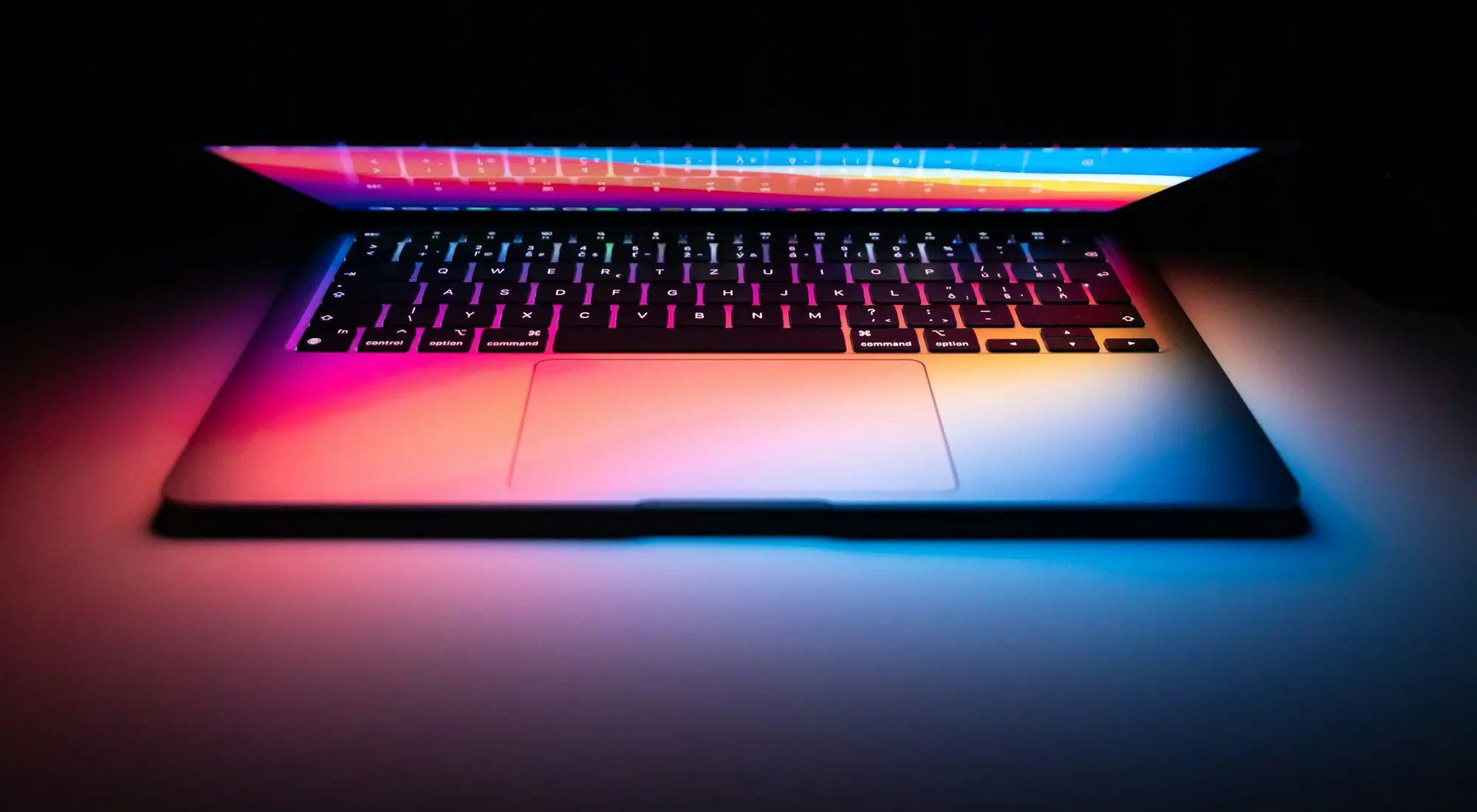 A MacBook screen lit up with a colourful wallpaper, seen from above.