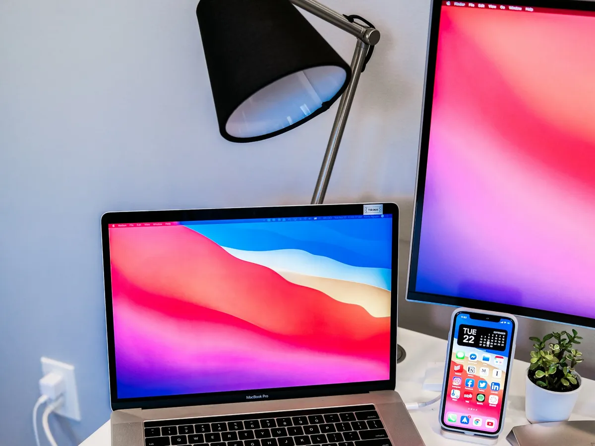 A laptop and a phone on a desk under a lamp, ready for a call.